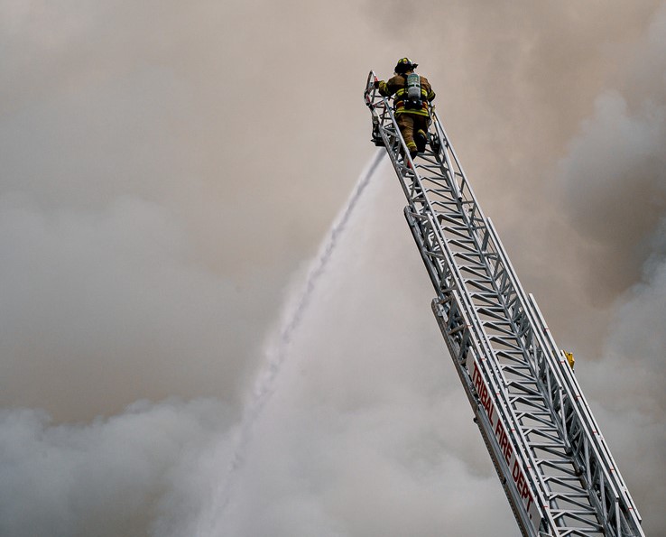 Firefighter On Ladder Spraying Hose